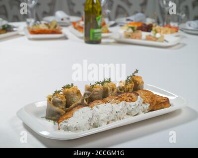 Fischkuchen mit weißer Soße und Fischfilet-Rollen, gefüllt mit Käse und Kräutern auf einem Teller auf weißem Hintergrund. Meeresfrüchte Stockfoto