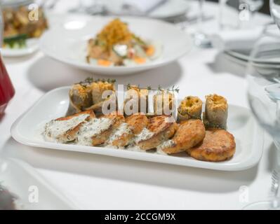 Fischkuchen mit weißer Soße und Fischfilet-Rollen, gefüllt mit Käse und Kräutern auf einem Teller auf weißem Hintergrund. Meeresfrüchte Stockfoto