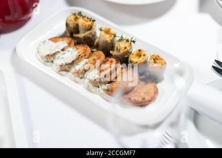 Fischkuchen mit weißer Soße und Fischfilet-Rollen, gefüllt mit Käse und Kräutern auf einem Teller auf weißem Hintergrund. Meeresfrüchte Stockfoto