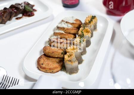 Fischkuchen mit weißer Soße und Fischfilet-Rollen, gefüllt mit Käse und Kräutern auf einem Teller auf weißem Hintergrund. Meeresfrüchte Stockfoto