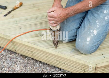 Nahaufnahme von Menschenhänden Bohren, um hölzerne Terrasse zu machen Zu Hause für den Garten während des Schließens Stockfoto