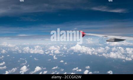 Flugzeugreisekonzept: Ansicht vom Flugzeugfenster. Wolken und blauer Himmel unter dem Flugzeugflügel, wie durch das Fenster eines Flugzeuges in breitem Engel mit KOP zu sehen Stockfoto