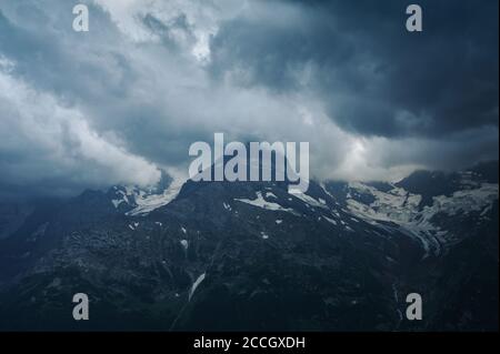 Düstere Berglandschaft mit donnerndem bewölktem Himmel, felsigen Bergketten und Gipfeln mit Gletschern und Schneefeldern. Regnerischer Tag in wilder Natur. Belalakaya, Dom Stockfoto