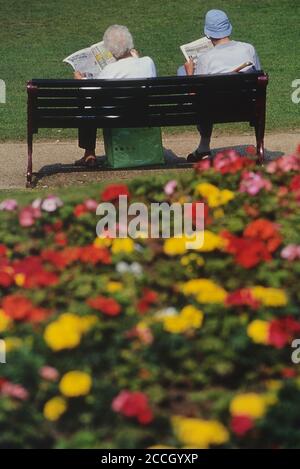 Ein älteres Paar, das Zeitungen liest, sitzt auf einer Parkbank. Tower Gardens, Skegness, Lincolnshire, England, Großbritannien Stockfoto