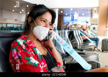Barcelona, Spanien - 20. august 2020: Eine junge Frau sitzt im Flughafen mit Gesichtsmaske, Gespräch am Telefon unterwegs, während einer Coronavirus globalen pande Stockfoto