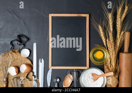 Leere Tafel und frische Eier, Kuchenmehl mit Küchenutensilien für Gebäck auf schwarzem Tisch, Kopierraum für Eingabemenü Text Stockfoto