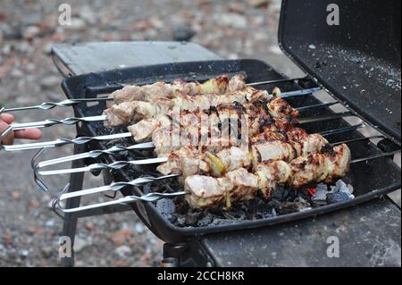 Mann's Hand drehen über Kebabs auf einem Grill für besser Qualität der Vorbereitung Stockfoto