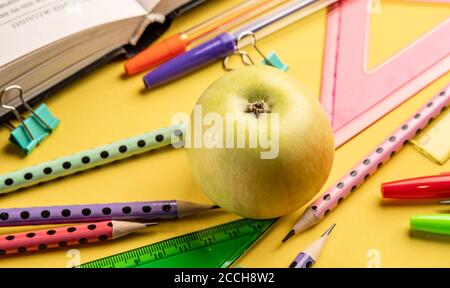 Apfel-, Buch- und bunte Schulpapiere auf gelbem Hintergrund. Zurück zur Schule Konzept Stockfoto