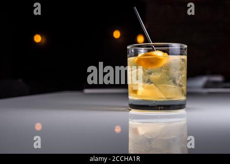 Ein Craft-Cocktail, der in Glas mit Stroh und Orangenschalen serviert wird, wird in moderner, cooler Bar-Atmosphäre serviert Stockfoto