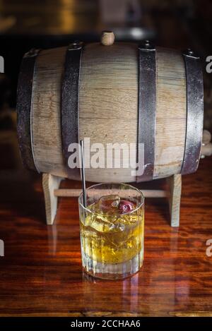 Eine rustikale Barszene mit einem klassischen Craft-Cocktail aus Bourbon-Whiskey und einem Fass auf der Holzbar. Stockfoto