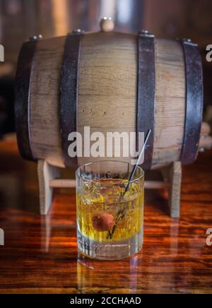 Vorne sitzt ein klassischer Cocktail aus Bourbon Whiskey Von einem Fass an einer rustikalen Bar Stockfoto