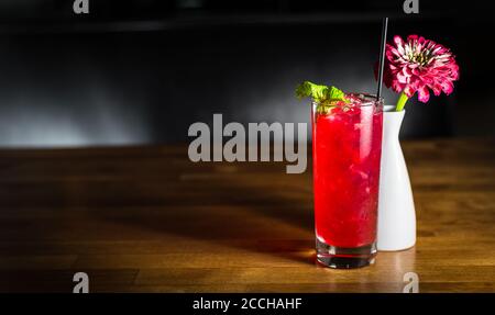 Ein Craft-Cocktail in einem Collins-Glas daneben Eine Blumenvase in einer eleganten Bar-Umgebung Stockfoto