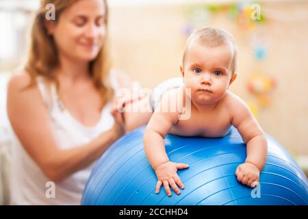 Seitenansicht der jungen kaukasischen Mutter hilft kleinen Baby trägt Windel üben Gymnastik Übungen zu Hause. Glückliche Frau Ausbildung Kind mit großen BL Stockfoto