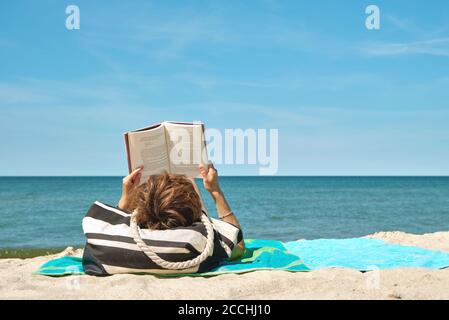 Kaukasische Frau liegt am Strand und liest ein Buch Heller Sommertag Stockfoto