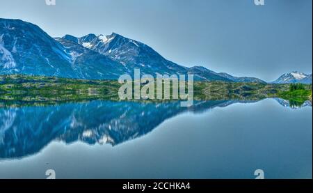 Das Bild wurde in Yukon, Kanada, aufgenommen, das die zerklüftete Bergkette an klaren, sonnigen Tagen in ruhigem und stillem Wasser widerspiegelt. Stockfoto