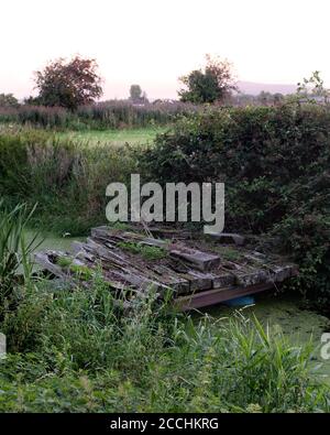 August 2020 - Alte verfaulte Brücke über einen Entwässerungsgraben, aus Eisenbahnschwellen Stockfoto