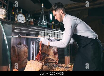 Der Kellner oder Koch bekommt trockenes Fleisch im Kühlschrank. Stockfoto