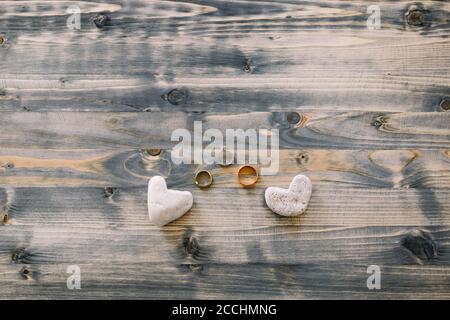 Eheringe für Braut und Bräutigam und ein Ring aus Weißgold mit herzförmigen Steinen auf einem Holzhintergrund. Stockfoto