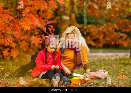 Glückliche Mutter traf ihre kleine Tochter nach dem Unterricht. Kinder lesen Bücher im Freien Grundschule. Stockfoto
