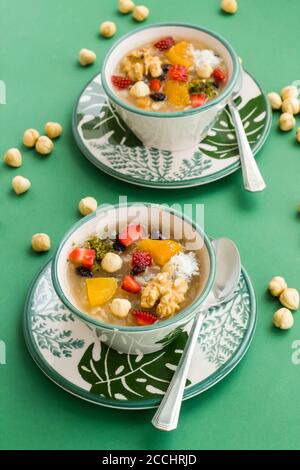 Traditionelles türkisches Dessert Ashura oder Noah's Pudding in stilvollen grünen Schalen auf grünem Hintergrund mit Haselnüssen. Stockfoto