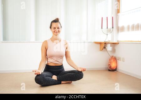 Die ganze Länge der schönen europäischen Frau sitzt in Lotuspose Zu Hause Stockfoto