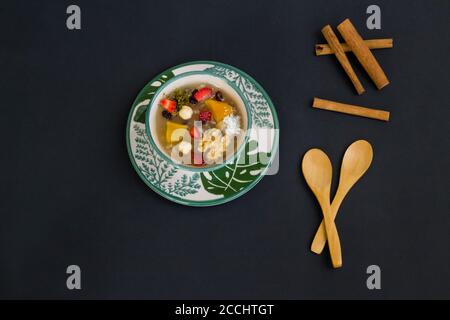 Traditionelles türkisches Dessert Noah's Puding in stilvoller grüner Schale auf schwarzer Oberfläche mit Löffel und Kopierraum.Draufsicht. Stockfoto