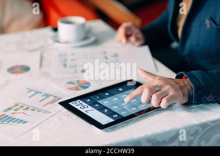 Nahaufnahme der Hand EINES Geschäftsreisenden, der Bill on Digital Tablet over Desk analysiert. Stockfoto