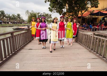 Hoi An / Vietnam - January 18, 2020: group portrait of young vietnamese women dressed in colorful dresses on wooden bridge in historic center Stock Photo