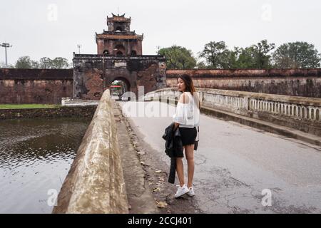 Hue / Vietnam - 20. Januar 2020: Hübsche junge Vietnamesin besucht die Kaiserstadt Hue vor dem Eingang zu den Mauern Stockfoto