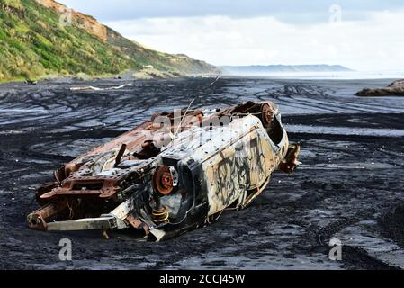 Ein Auto von Flut gefangen und verlassen auf schwarzem Sand von Karioitahi Strand, Neuseeland. Autowrack in schwarzem Sand vergraben, halb in Sand getaucht. Stockfoto