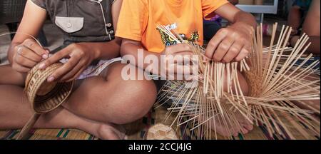 Zwei asiatische Mädchen machten Bambus-Korbflechterei im Hinterhof, sie machten traditionelle Korbflechterei für ihren Lebensunterhalt. Mukdahan, Thailand. Nahaufnahme. Konzentrieren Sie sich auf die Hände. Stockfoto