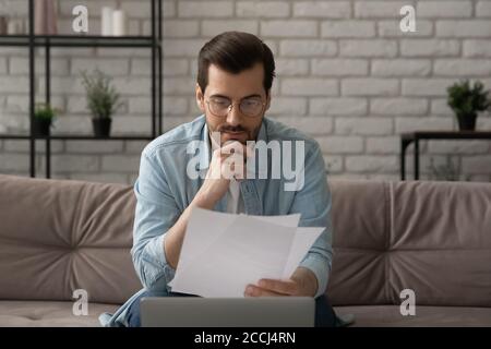 Pensive kaukasischen Mann arbeiten auf Laptop lesen Papierdokumente Stockfoto