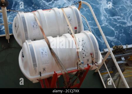 Zwei Liferafts, die mit weißen Bändern in der roten Wiege auf dem Frachtschiff von der rechten Seite des Aufbaus gesichert sind. Stockfoto