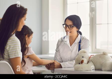 Die Patienten der Familie werden von einem Hausarzt in einer medizinischen Klinik konsultiert. Ärztin lächelt das Mädchen an und ihre Mutter sitzt am Tisch im Stockfoto