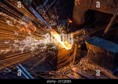 Schmied das geschmolzene Metall auf dem Amboss manuell mit schmieden Funkenfeuerwerk Stockfoto