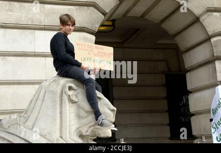 Junger Mann, saß auf Steinlöwe, mit Protestplakat. Stockfoto