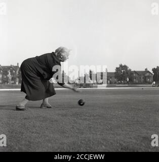 1950er Jahre, historisch, in einem offenen Bereich, draußen auf einem Rasen, eine Dame mittleren Alters Biegen über Rollen einen schweren Ball, spielen eine Sportart bekannt als Schüsseln oder Rasenschalen, gespielt auf flach eng geschnittenem Gras, eine glatte Oberfläche als grün bekannt, England, Großbritannien. Stockfoto