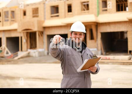 Amerikanischer Baumeister, der Wohnungsschlüssel gab und Zeichnungsplan im Notizbuch hielt. Stockfoto