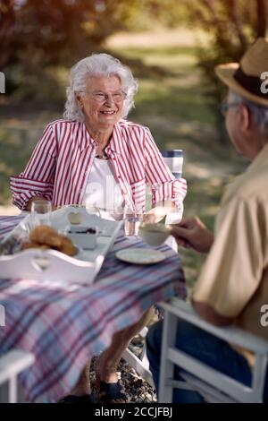 Lächelndes Senioren-Paar, das draußen am Tisch sitzt. Ältere Frauen und Männer genießen zusammen und trinken Kaffee. Stockfoto
