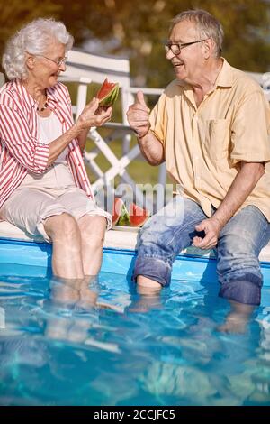 Romantische glückliche ältere Mann und Frau genießen im Sommerurlaub in der Nähe von Schwimmbad und essen Wassermelone. Stockfoto