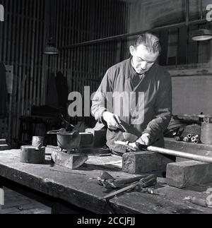 50er Jahre, historischer Mann mittleren Alters in Overalls in einer Transportwerkstatt oder einem großen Schuppen bei Great Wester Railways, der Flüssigkeit auf einen langen Metallstab gießt, England, Großbritannien. Stockfoto