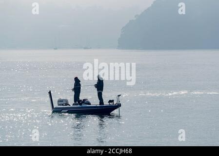 An einem nebligen Wintermorgen stehen zwei Männer in einem Kleines offenes Fischerboot in der Nähe von Cockatoo Island mit Angelruten Im ruhigen Hafenwasser Stockfoto