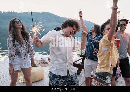 Gruppe von jungen glücklichen Menschen mit Wunderkerzen tanzen während an Party an der frischen Luft Stockfoto