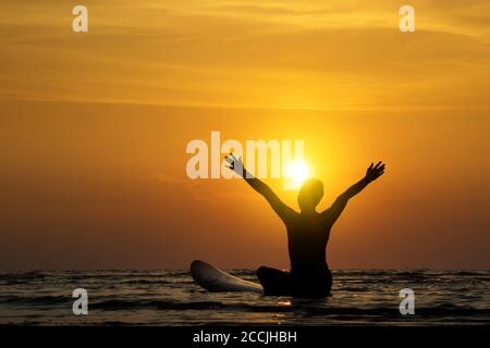 Silhouette des Surf-Mann sitzen auf einem Surfbrett, offene Arme. Surfen am Strand bei Sonnenuntergang. Outdoor Wassersport Abenteuer Lifestyle.Sommer Aktivität. Schönes Asien Stockfoto