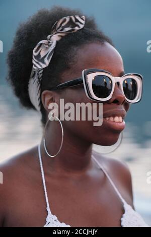 Afrikanische junge lächelnde Frau in Sonnenbrille im Freien auf Party stehen Stockfoto
