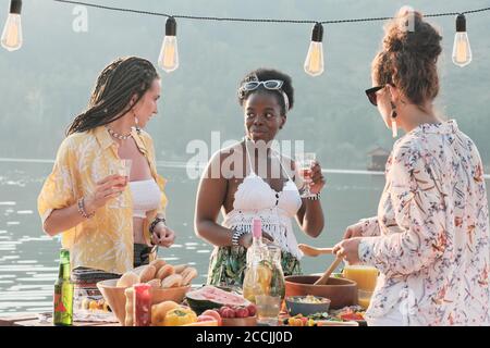 Junge schöne Frauen stehen neben dem Esstisch und reden Zueinander essen sie im Freien zu Mittag Stockfoto