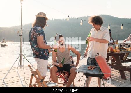 Gruppe junger Männer, die Bier trinken und mit jedem sprechen Andere während der Party auf einem Pier Stockfoto