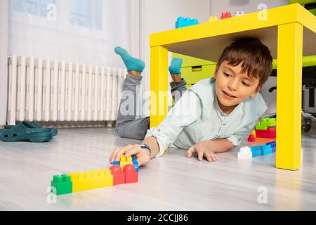 Junge spielen mit Blöcken unter dem Tisch im Kinderzimmer Auf dem Boden Stockfoto