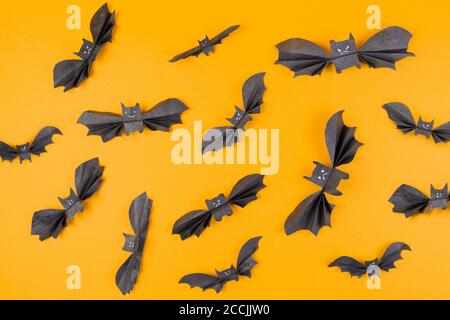 Viele Fledermäuse aus Papier auf orangefarbenem Hintergrund. Flach liegend. Das Konzept von Halloween und Feiertagsdekorationen. Stockfoto