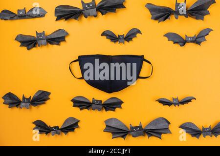 Wiederverwendbare schwarze Anti-Virus-Maske von Papier Fledermäuse umgeben. Orangefarbener Hintergrund. Flach liegend. Das Konzept des Schutzes vor dem Virus an Halloween. Stockfoto